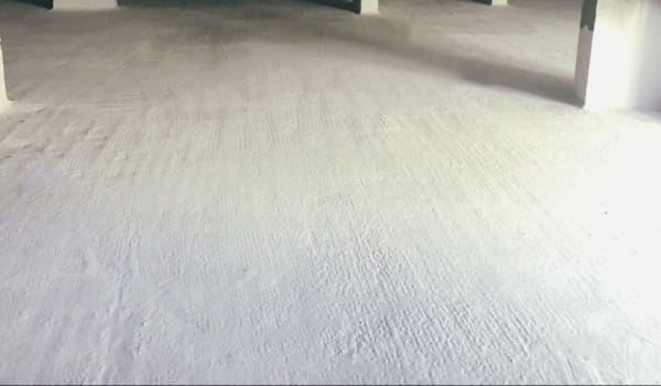 Підземний паркінг з текстурованою бетонною підлогою, колонами та обмазувальною гідроізоляцією білого кольору.