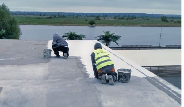 Двоє працівників Білдкрафт проводять гідроізоляцію плоского даху біля водойми.