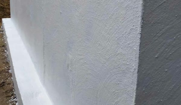 Вид зблизька текстурованого білого кута стіни, з нанесеною гідроізоляцією білого кольору.